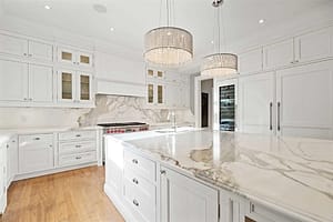 This all white Freehold install includes large crystal lights hover over a full slab kitchen center island and matching backsplash made of marble.